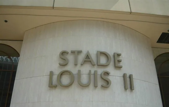 Biển hiệu lớn mang tên &quot;Stade Louis II&quot; màu trắng nổi bật trên nền đá, chào đón những người hâm mộ đến với thánh địa bóng đá của Monaco.