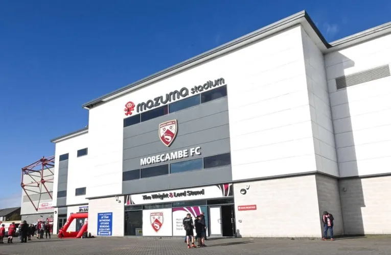 Cổng chính sân Mazuma Mobile Stadium, nơi những người hâm mộ lặng lẽ bước vào thế giới bóng đá của Morecambe