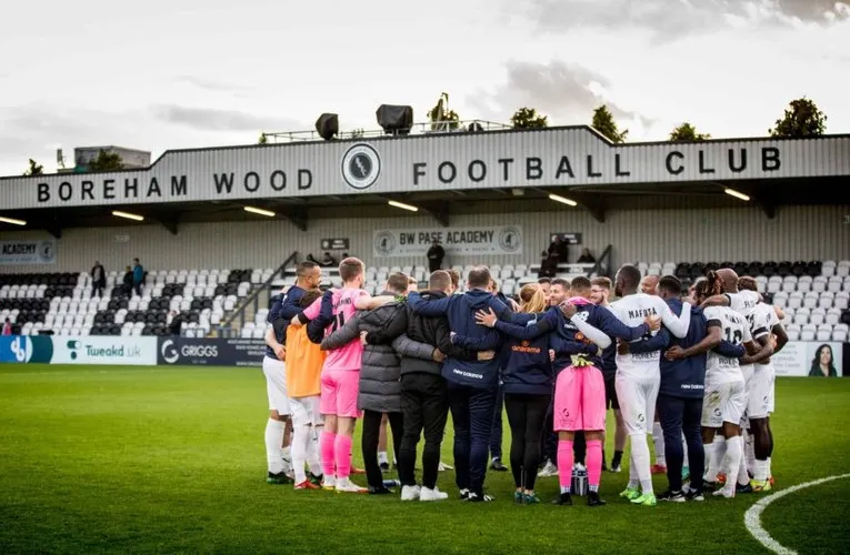 Đội hình Boreham Wood FC đứng trước khán đài chính tại Meadow Park, biểu tượng của sự kiên cường