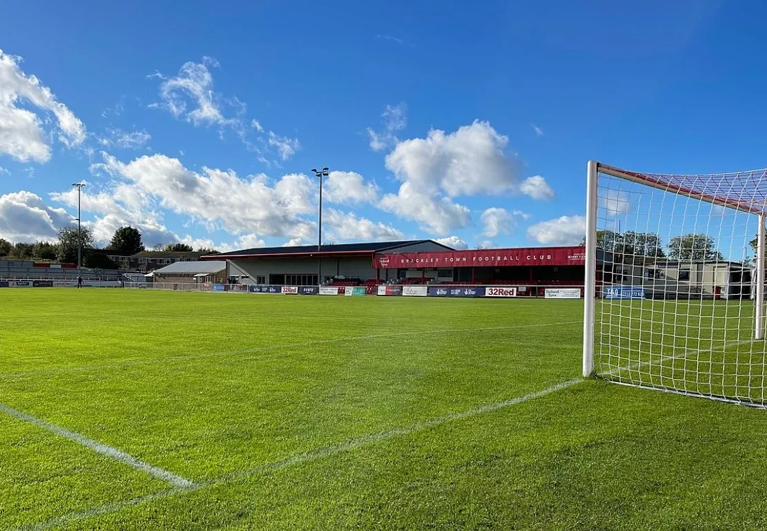 Khán đài chính (Main Stand) của St James Park Brackley, nơi ánh đèn hiu hắt soi rọi những ghế ngồi đơn sơ.