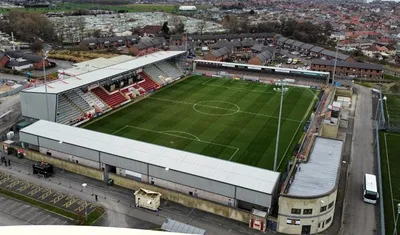 Toàn cảnh sân vận động Mazuma Mobile từ trên cao, hiện đại và yên bình trong buổi chiều Morecambe