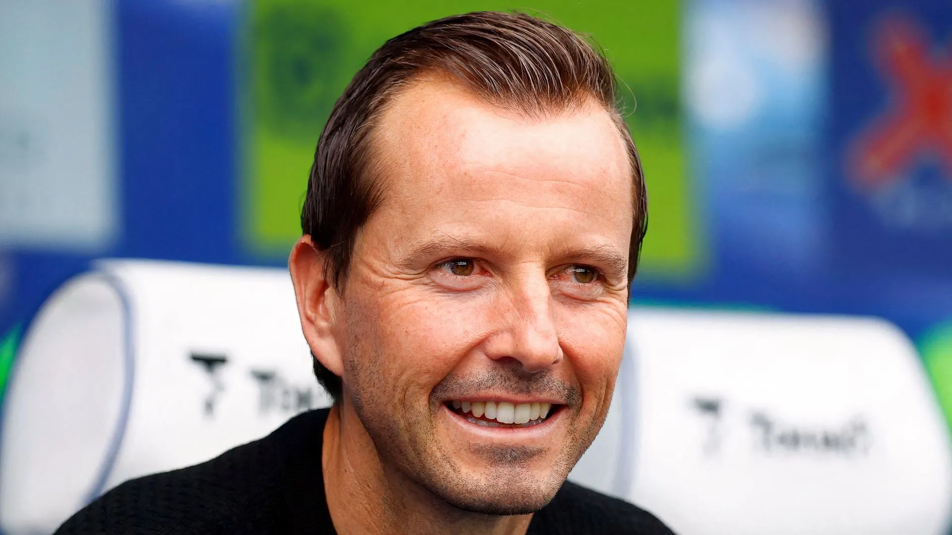 Một huấn luyện viên đứng lặng lẽ trên đường pitch, ánh mắt đăm chiêu, thể hiện sự lo lắng hoặc suy tư về chiến lược trong một trận đấu căng thẳng của Giải Hạng Nhất Anh.